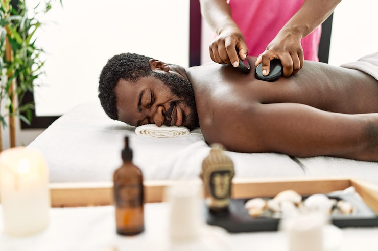 Photo homme afro-américain recevant un massage du dos avec des pierres noires au centre de beauté.
