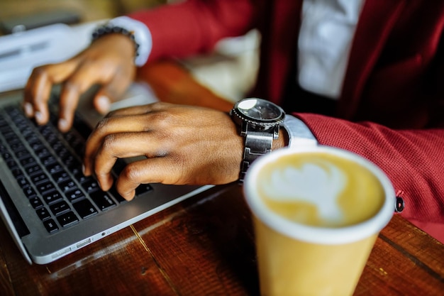 Un homme afro-américain reçoit une éducation en ligne et boit du café pour aller dans une tasse écologique en papier