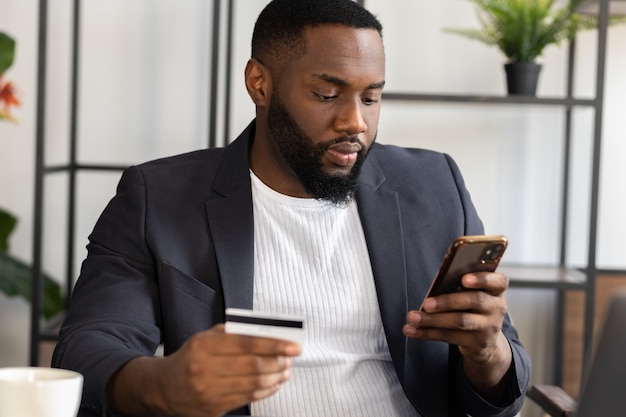 Un homme afro-américain s'assoit à table pour faire des achats en ligne avec une carte de crédit sur un smartphone