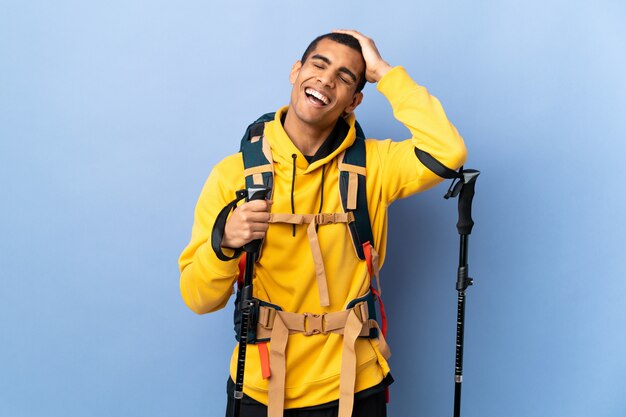 Homme afro-américain avec sac à dos et bâtons de randonnée sur un mur isolé en riant