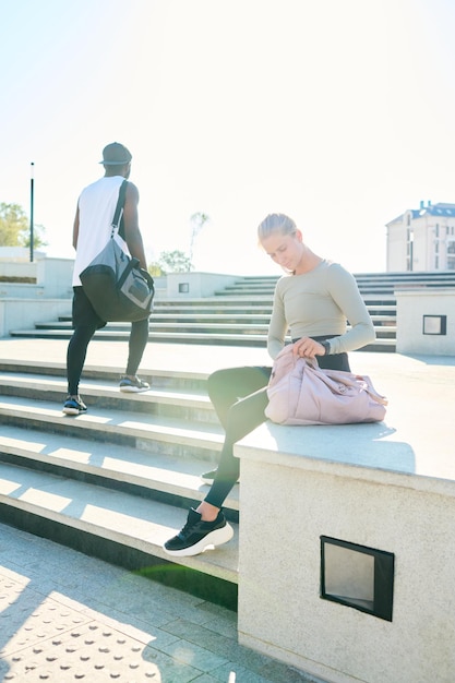 Homme afro-américain avec sac de sport passant par une fille assise sur un bord en béton