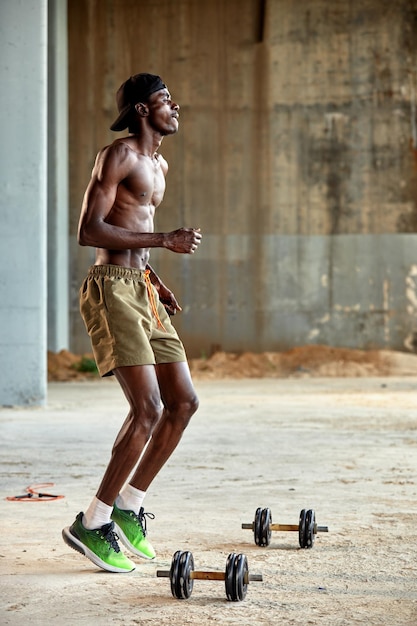 Homme afro-américain séduisant souriant et faisant de l'exercice avec des haltères