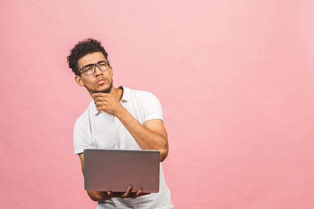 Homme afro-américain sérieux réfléchi avec ordinateur portable isolé sur fond rose