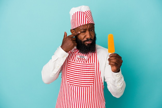 Homme afro-américain de sorbetière tenant une glace isolée sur fond bleu montrant un geste de déception avec l'index.