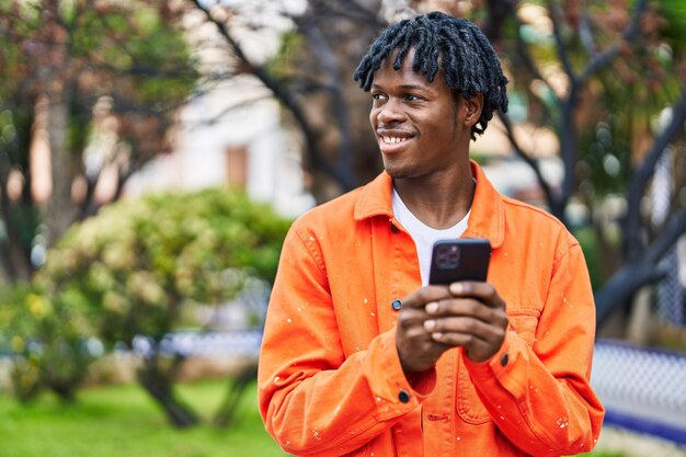 Homme afro-américain souriant confiant à l'aide de smartphone au parc