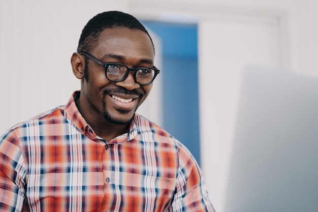 Homme afro-américain souriant dans des verres travaillant en ligne sur un ordinateur portable lisant des e-mails avec de bonnes nouvelles