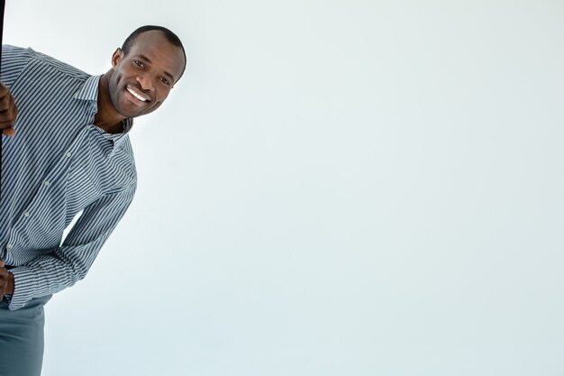 Homme afro-américain souriant positif se sentir heureux tout en se cachant contre un mur blanc