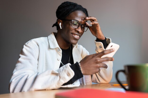 Un homme afro-américain souriant et réussi tenant un téléphone utilise des applications mobiles divertissantes ou des médias sociaux