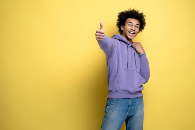 Homme afro-américain souriant tenant le pouce vers le haut isolé sur fond jaune, espace de copie