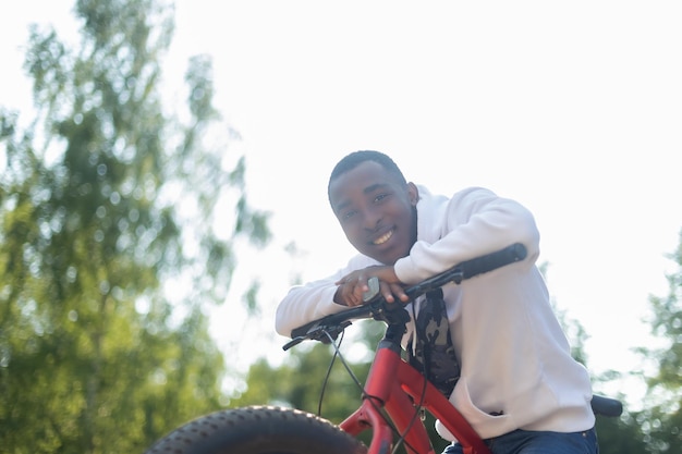 Un homme afro-américain souriant avec un vélo dans un parc public Sports et loisirs