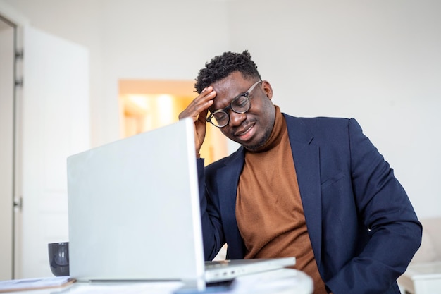 Homme afro-américain stressé et fatigué touchant les tempes souffrant de maux de tête après de longues heures de travail surmené homme d'affaires débordé assis au bureau se sentant mal