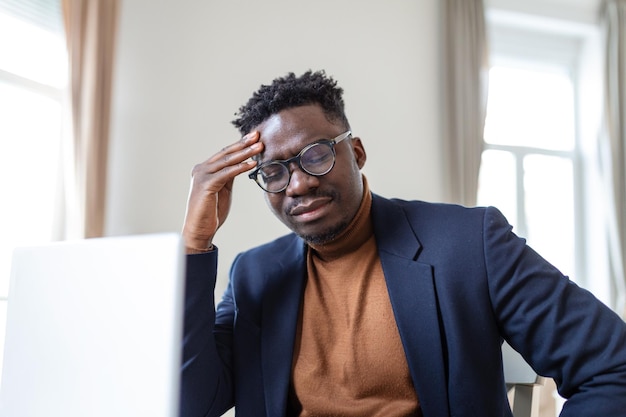 Homme afro-américain stressé et fatigué touchant les tempes souffrant de maux de tête après de longues heures de travail surmené homme d'affaires débordé assis au bureau se sentant mal