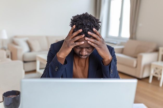 Homme afro-américain stressé et fatigué touchant les temples souffrant de maux de tête après de longues heures de travail surmené homme d'affaires débordé assis au bureau se sentant mal