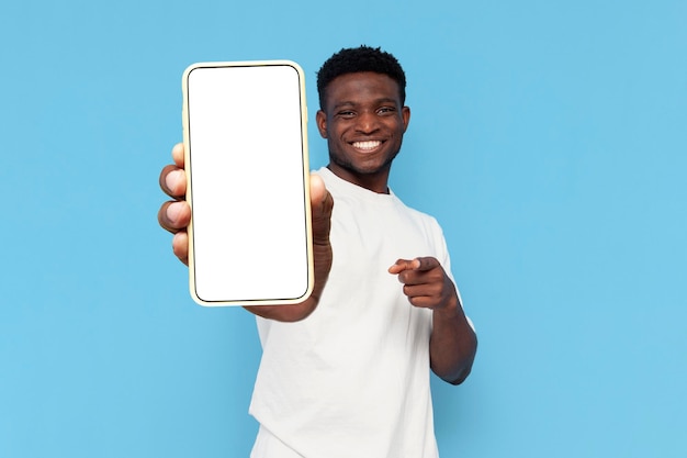 un homme afro-américain en t-shirt blanc montre un écran de smartphone vierge sur fond bleu isolé