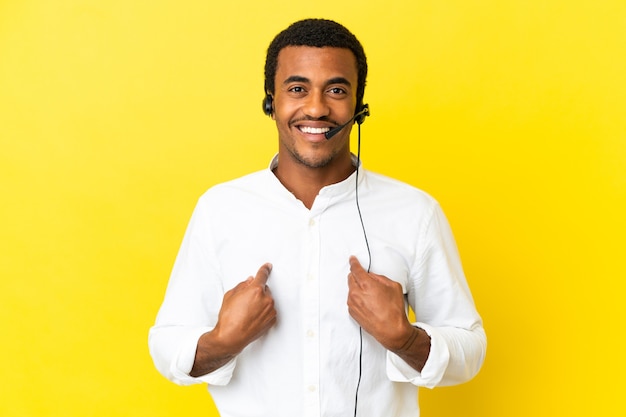 Homme afro-américain de télévendeur travaillant avec un casque sur fond jaune isolé avec une expression faciale surprise