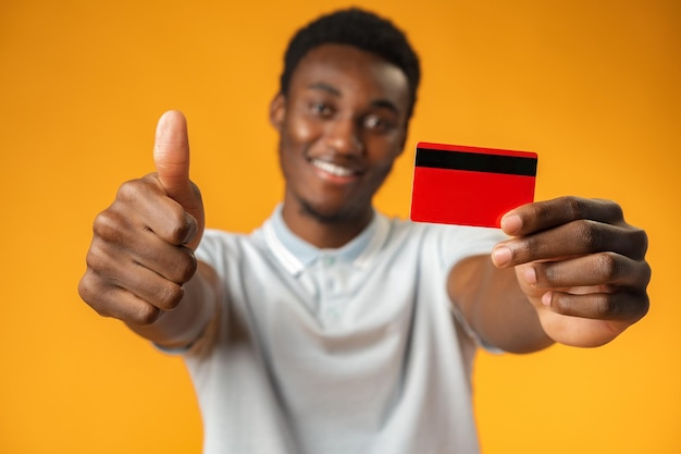 Homme afro-américain tenant une carte de crédit rouge sur fond jaune en studio