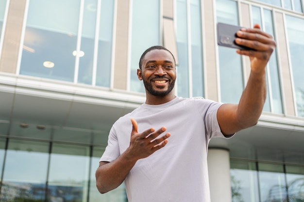 Homme afro-américain tenant un smartphone ayant un chat vidéo dans une rue urbaine dans un blogueur de la ville