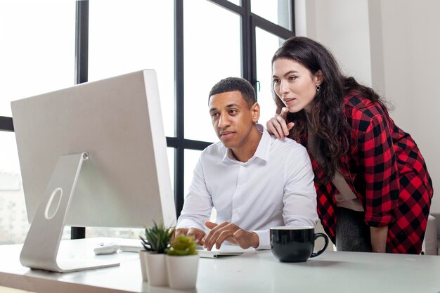 Un homme afro-américain en vêtements d'affaires et lunettes est assis et travaille à l'ordinateur avec sa femme