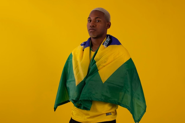 Homme afro-brésilien supporter de l'équipe de football brésilienne dans la coupe 2022 avec le drapeau du Brésil et avec des expressions faciales