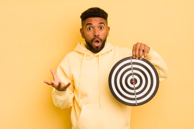 Photo un homme afro cool étonné, choqué et étonné par un incroyable concept de cible de fléchettes surprise