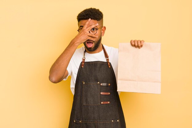 Un homme afro cool qui a l'air choqué, effrayé ou terrifié, couvrant le visage avec un livreur à la main et un concept de restauration rapide