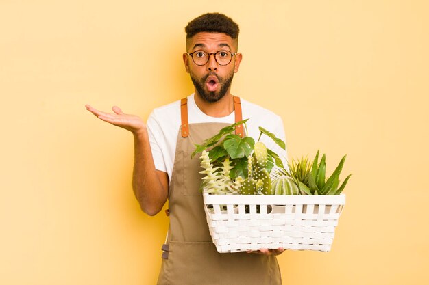 Un homme afro cool qui a l'air surpris et choqué avec la mâchoire tombée tenant un jardinier d'objets et un concept de plante