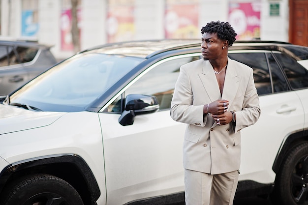 Homme afro élégant en costume beige old school contre une voiture suv électro hybride moderne