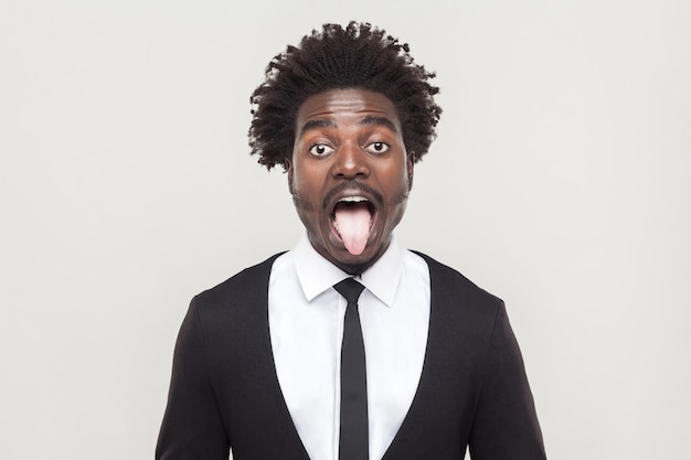 Homme afro fou regardant la caméra et la langue. Prise de vue en studio, fond gris