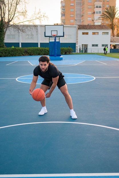 Homme afro-latin jouant au basket-ball faisant rebondir la balle sur un terrain au coucher du soleil