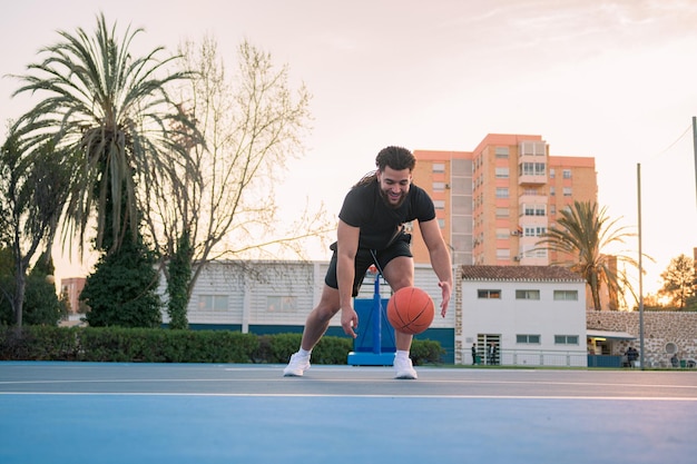 Homme afro-latin jouant au basket-ball faisant rebondir la balle sur un terrain au coucher du soleil