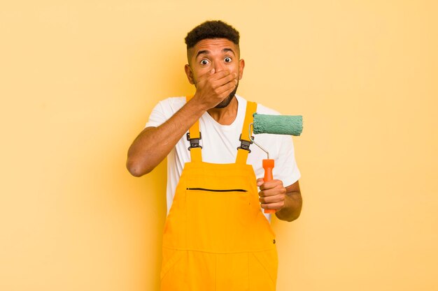 Homme afro noir couvrant la bouche avec les mains avec un concept de maison de peinture choqué