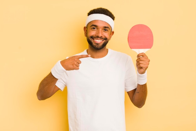 Homme afro noir souriant joyeusement se sentant heureux et pointant vers le concept de ping-pong latéral