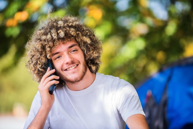 Un homme afro souriant assis dans la nature et parlant sur un smartphone. Photo de haute qualité