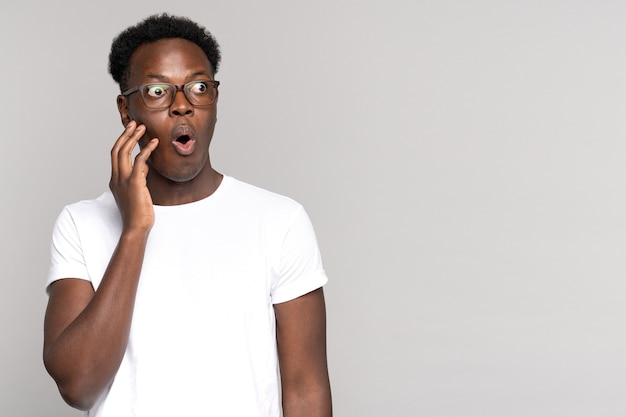 Un homme afro surpris ouvre de grands yeux, touchant son visage, choqué par des prix sans précédent