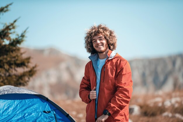 Un homme afro tôt le matin devant une tente de montagne prépare un sac à dos de voyage