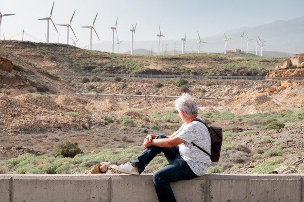 Un homme âgé actif assis à l'extérieur lors d'une journée de randonnée à la recherche d'une ferme de moulins à vent sur la montagne