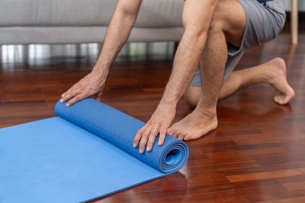 Homme âgé actif et sportif préparant un tapis d'exercice de remise en forme roulant sur le sol du salon à la maison Exercice à domicile comme concept de mode de vie corporel sain après la retraite Clout