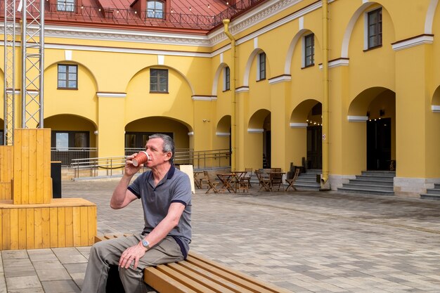 Un homme âgé adulte est assis sur un banc et boit du café