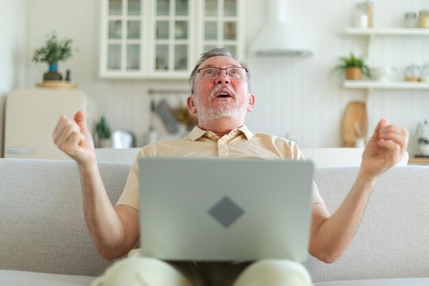 Un homme âgé d'âge moyen excité, un gagnant euphorique, un grand-père plus âgé qui regarde son ordinateur portable et lit.