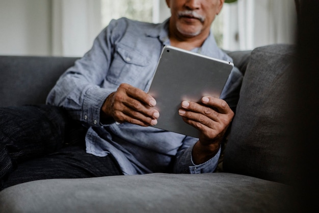 Homme âgé à l'aide d'une tablette sur un canapé