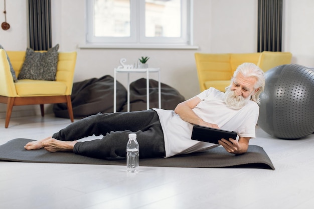 Homme âgé allongé sur un tapis de yoga et utilisant une tablette numérique