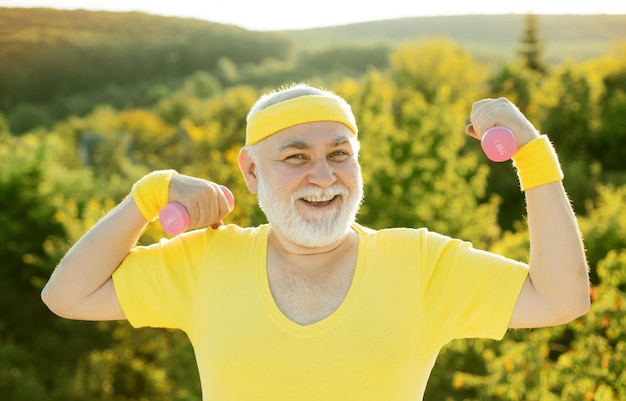 Homme âgé après son entraînement sportif senior heureux faisant de l'exercice avec des haltères de levage sur le parc verdoyant b