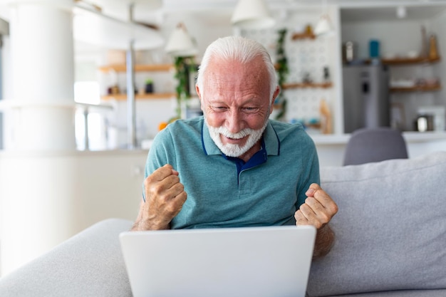 Un homme âgé assis sur un canapé regardant un écran d'ordinateur portable crier de joie se sent excité heureux de célébrer la victoire de la loterie moment chanceux a obtenu des opportunités de vente en ligne et des remises sur le concept de commerce électronique