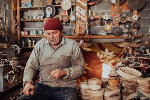 Un homme âgé assis dans l'atelier et traitant des ustensiles en bois à l'ancienne