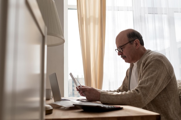 Homme âgé assis avec de la paperasse et utilisant une calculatrice tout en comptant de l'argent