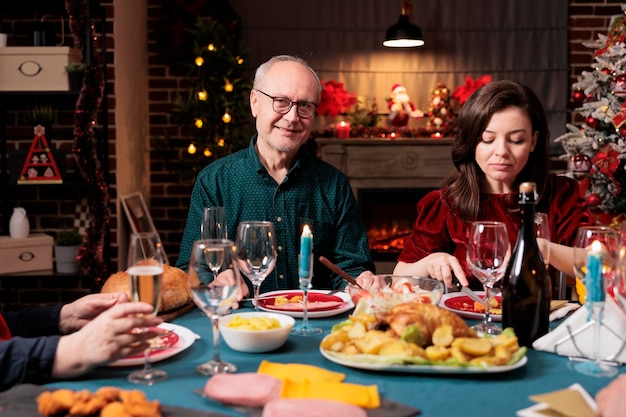 Homme âgé au dîner en famille, mangeant des plats délicieux et célébrant le réveillon de Noël à la maison. Grands-parents organisant un rassemblement festif pendant la célébration de la saison hivernale, décorations de Noël.