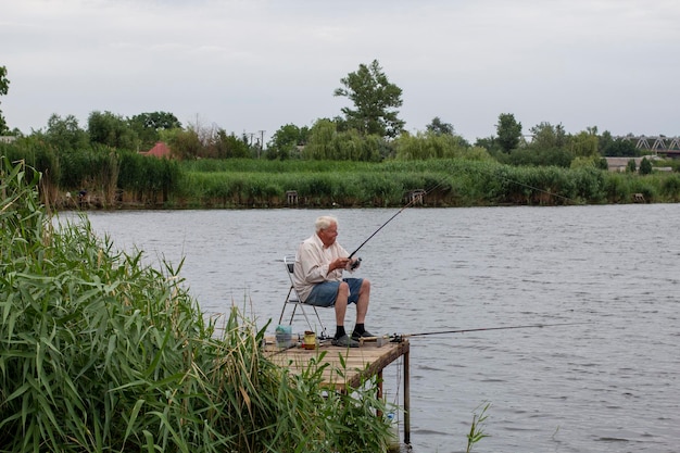 Homme âgé aux cheveux gris pêchant sur le lac dans la nature concept de patience et de relaxation pêcheur avec une canne à pêche dans la naturexAFêcheur assis et pêchant avec une cannexAMature