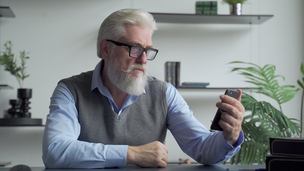 Un homme âgé avec une barbe grise utilise un smartphone au bureau