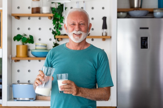 Homme âgé buvant un verre de lait avec un visage heureux debout et souriant Bel homme âgé buvant un verre de lait frais dans la cuisine