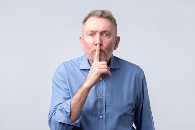 Homme âgé en chemise bleue faisant un geste de silence